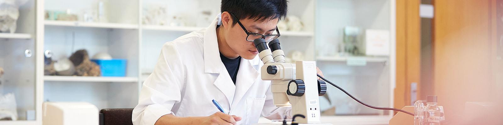 Science student examining item in microscope in a lab