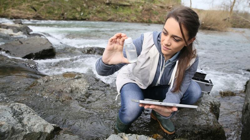 Scientist looking at water sample beside a river